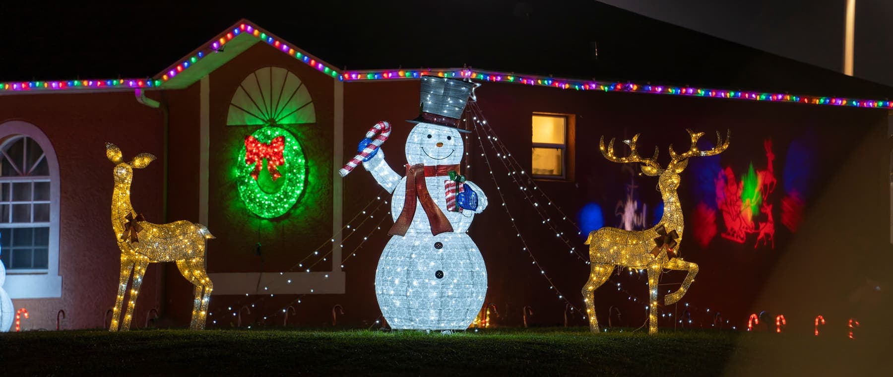 A house lit up at night with a glowing snowman, reindeer, wreath and colored lights
